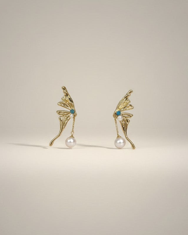 Gold wing-shaped earrings with pearls and turquoise stones on a light gray background