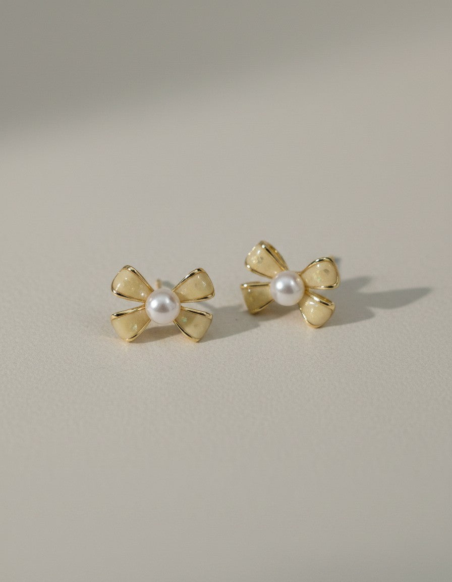 Muchichere bow-shaped stud earrings with faux pearls and creamy yellow enamel. Gold-tone metal.