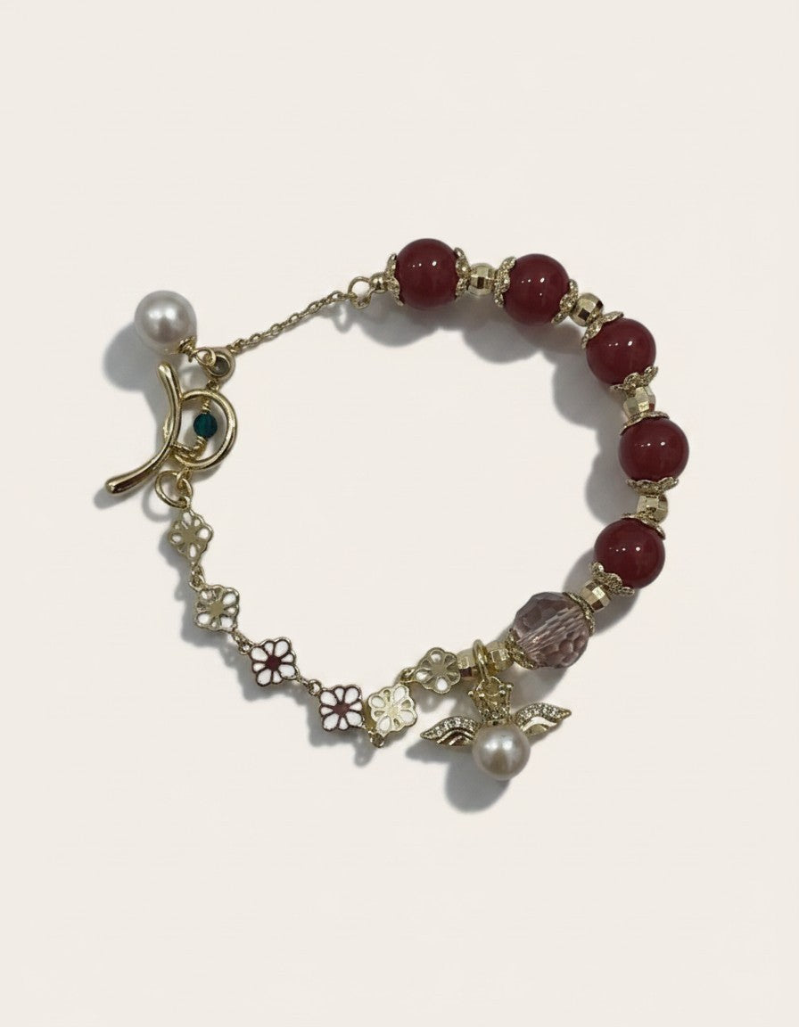 MuchieGold-tone bracelet with red agate beads, floral charms, and pearl angel charm.