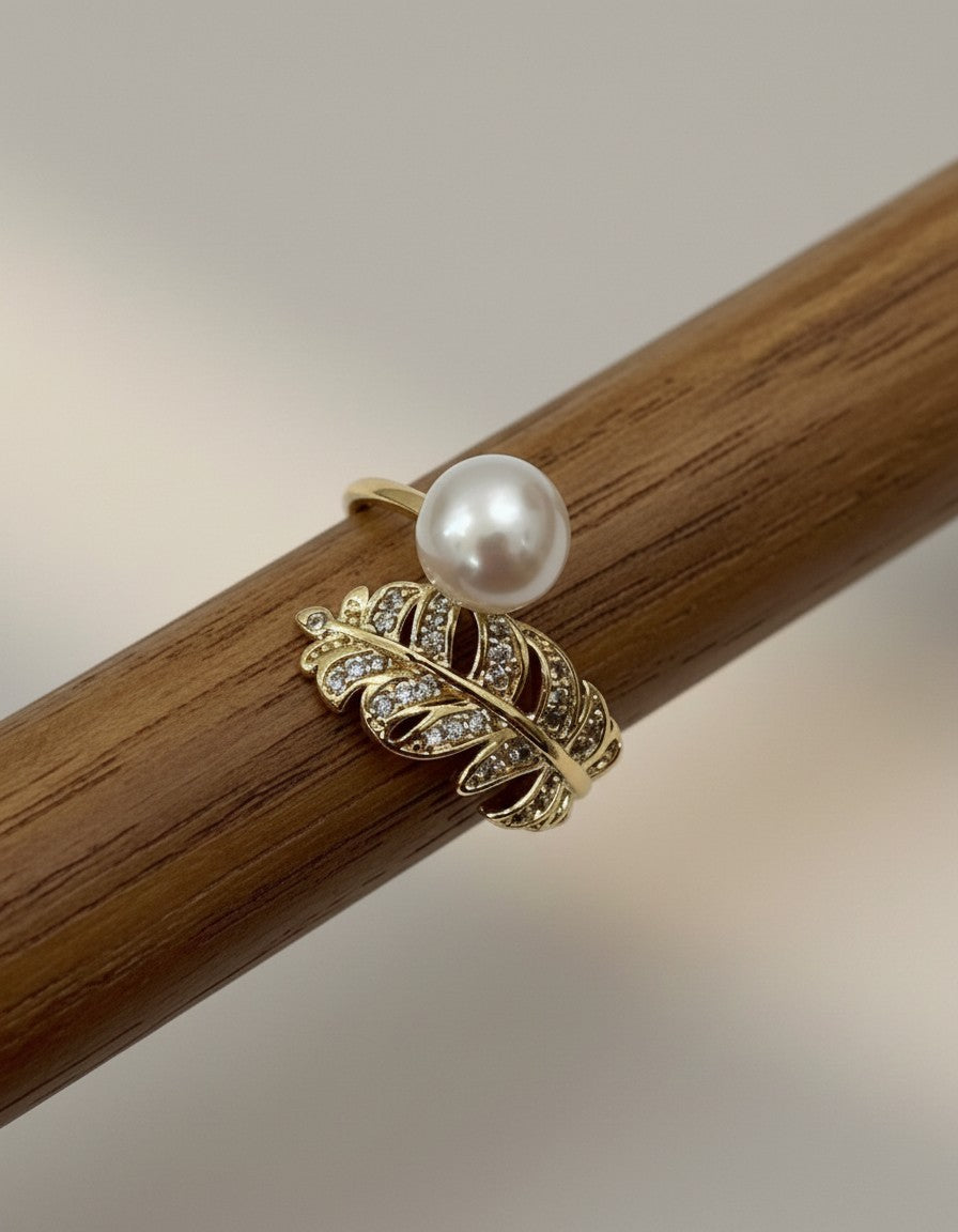 Muchier gold-tone adjustable ring with feather motif, pave cubic zirconia accents, and a dangling faux pearl.