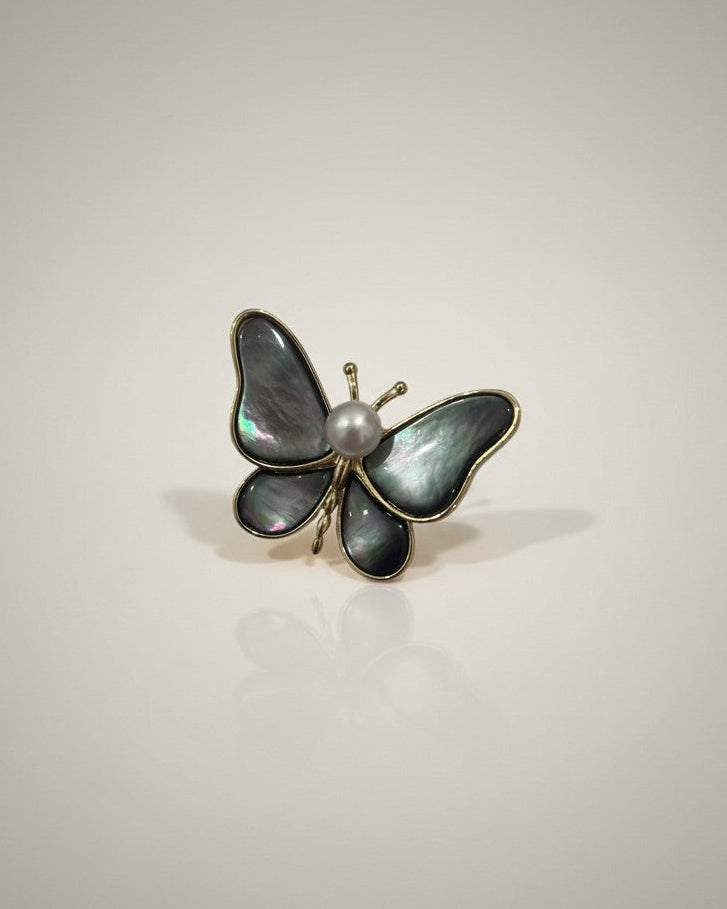 Butterfly-shaped brooch with pearl center on a light gray background