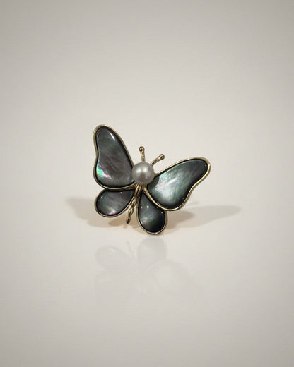 Butterfly-shaped brooch with pearl center on a light gray background