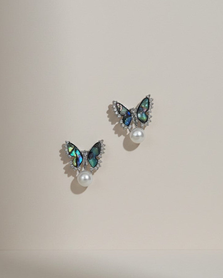 Butterfly-shaped earrings with gemstones and pearls on a beige background
