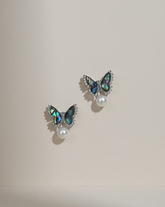Butterfly-shaped earrings with gemstones and pearls on a beige background