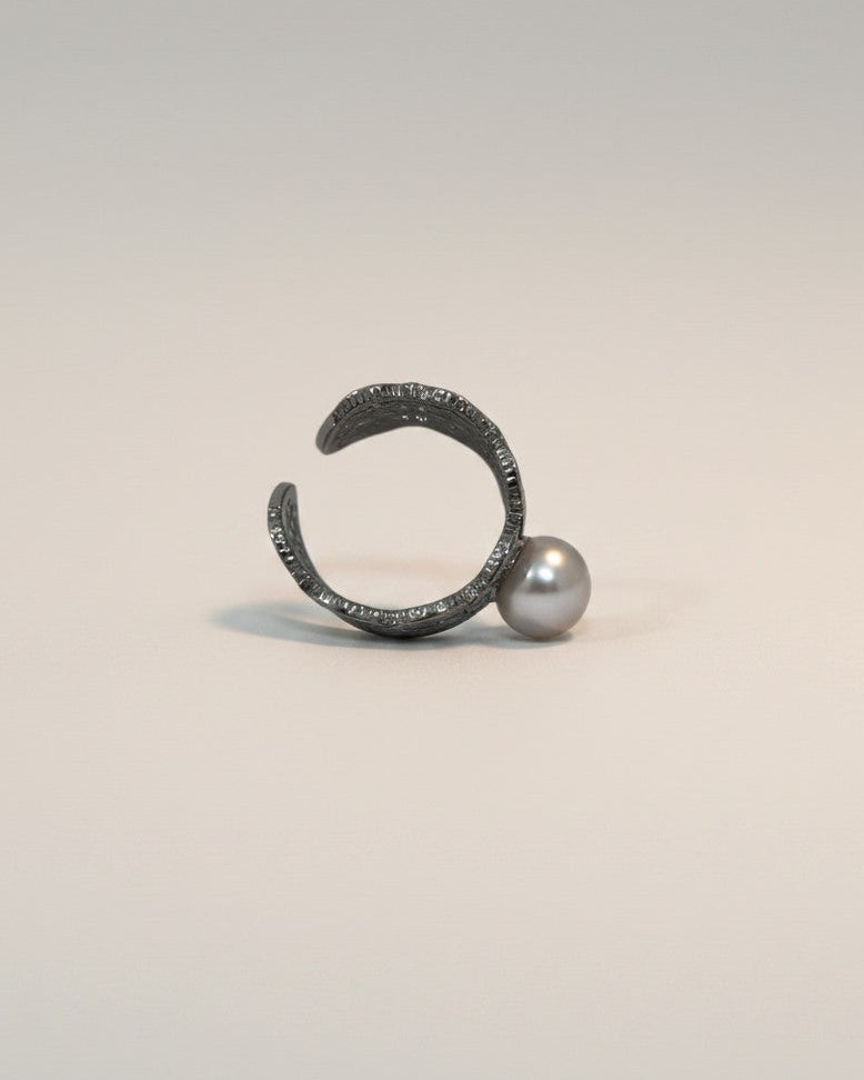 Metallic ring with a pearl on a light gray background