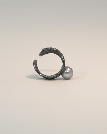 Metallic ring with a pearl on a light gray background