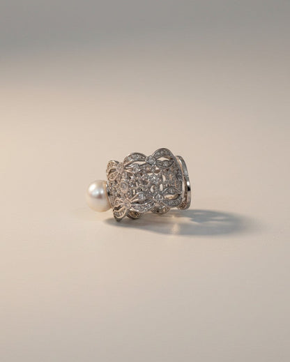 Silver ring with intricate design and pearl on a light gray background