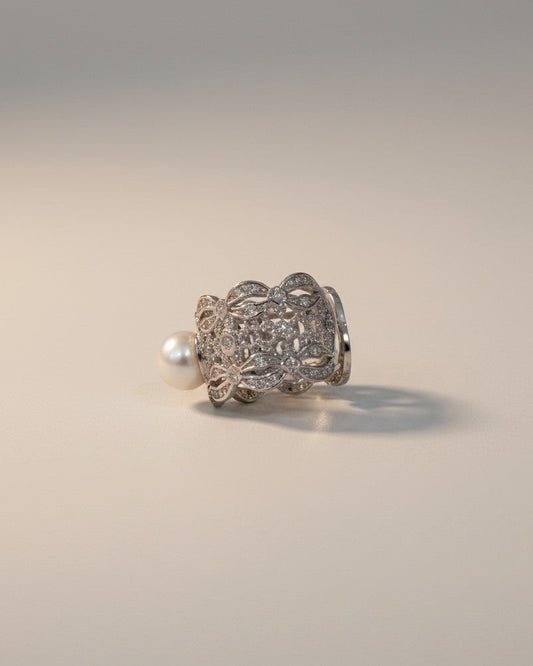 Silver ring with intricate design and pearl on a light gray background