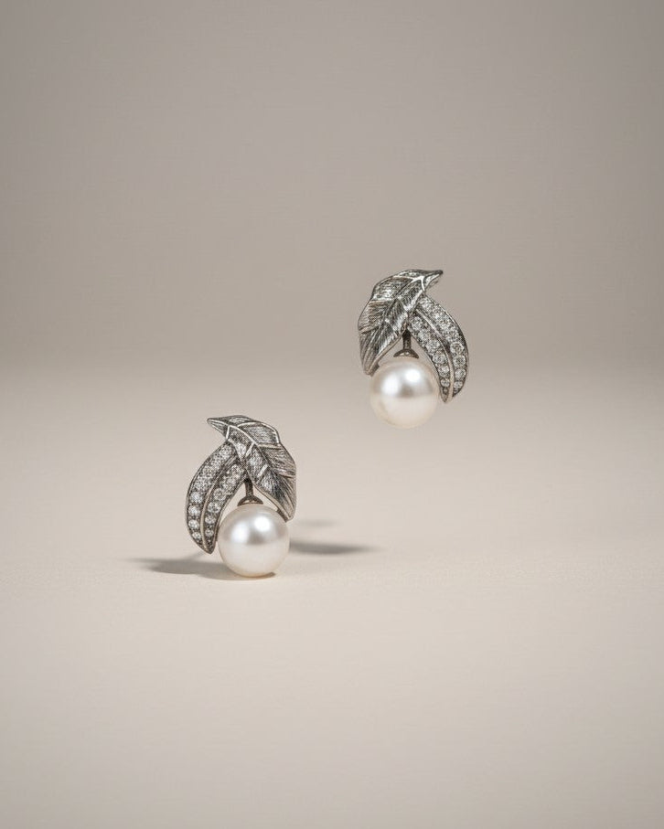 Pair of pearl earrings with silver leaves on a beige background