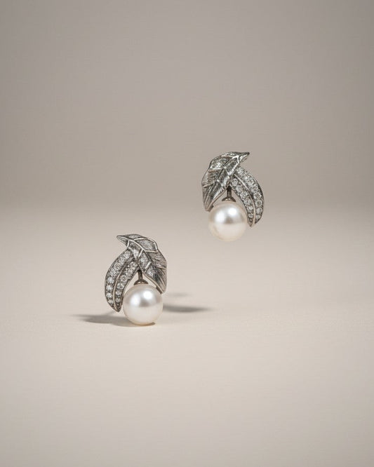 Pair of pearl earrings with silver leaves on a beige background
