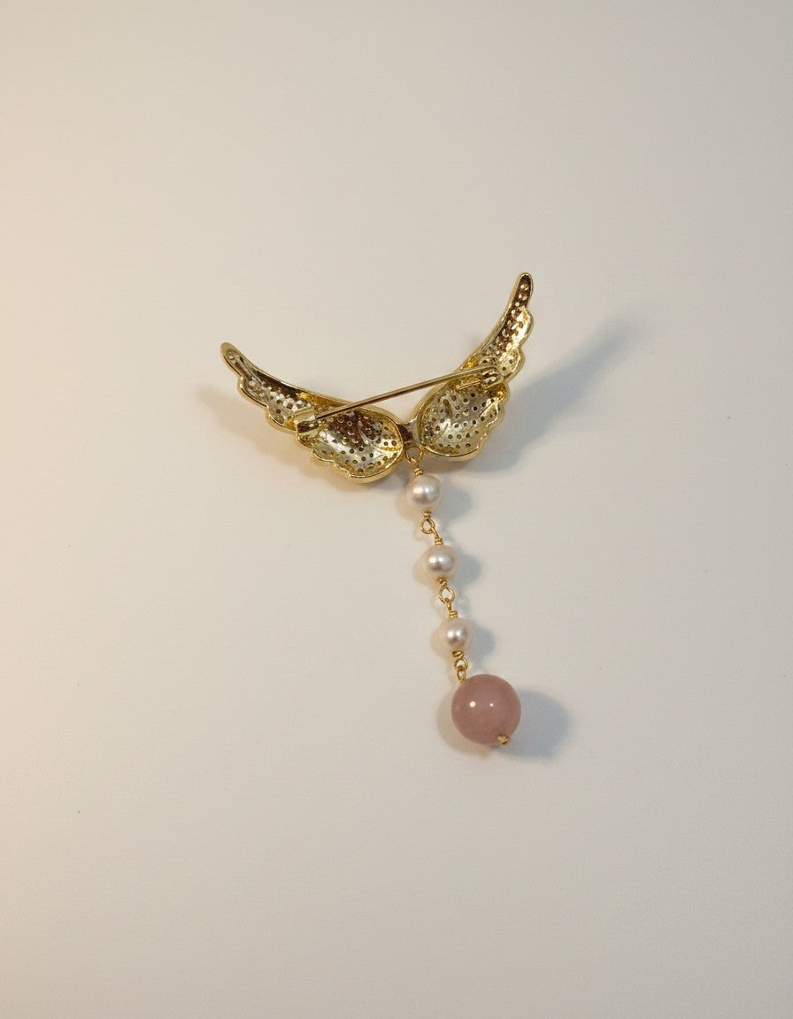 Muchic Angel wing brooch with pearls and rose quartz pendant. Gold-tone wings adorned with cubic zirconia, dangling pearls and rose quartz.