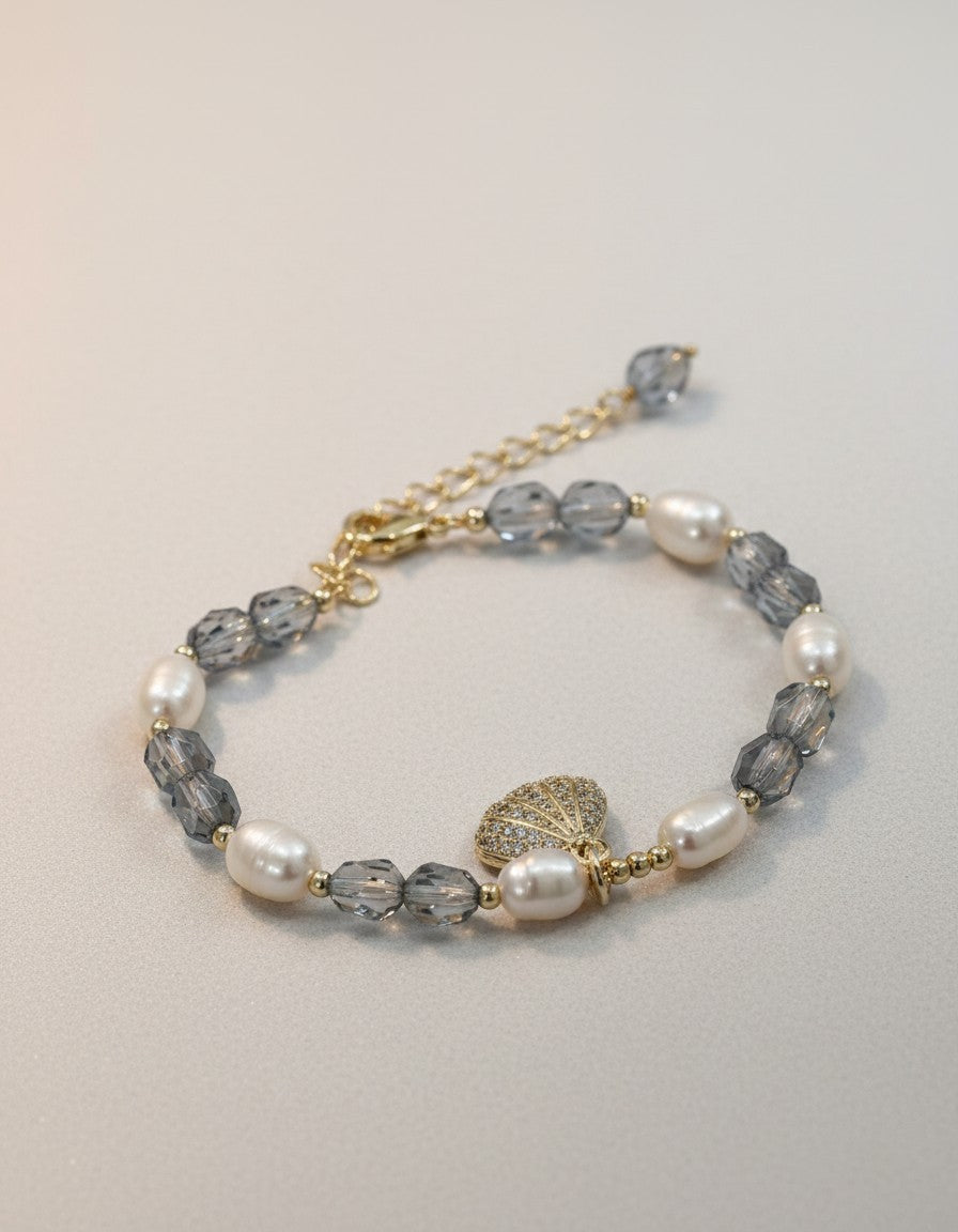 Muchic Pearl and Crystal Beaded Bracelet with Seashell Charm. Features freshwater pearls, grey crystal beads, and a CZ-encrusted seashell charm on a gold-tone chain.