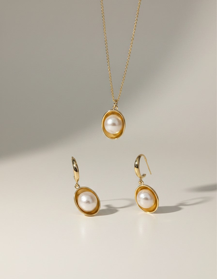 Muchier gold pearl pendant necklace and hoop earrings set. Lustrous pearls in polished gold bezels.